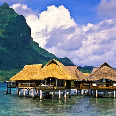 Overwater bungalows below a green volcanic peak in French Polynesia