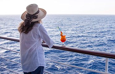 Woman in a sun hat with a drink at a cruise ship rail